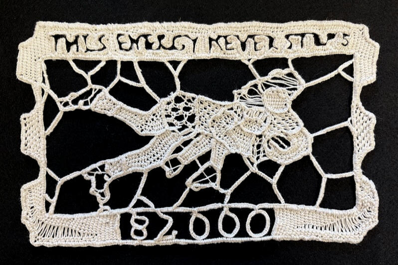A natural cotton needle lace textile piece depicting a ticket stub with the text "This Energy Never Stops" and the number 82,000. It also contains the image of a tackle in the middle.